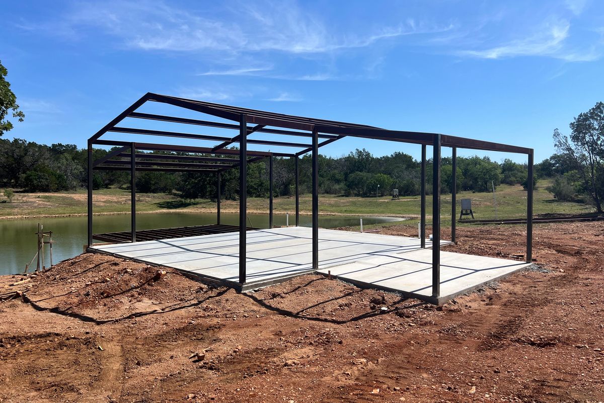 Steel-framed barndominium build on a slab above a Hill Country stock tank